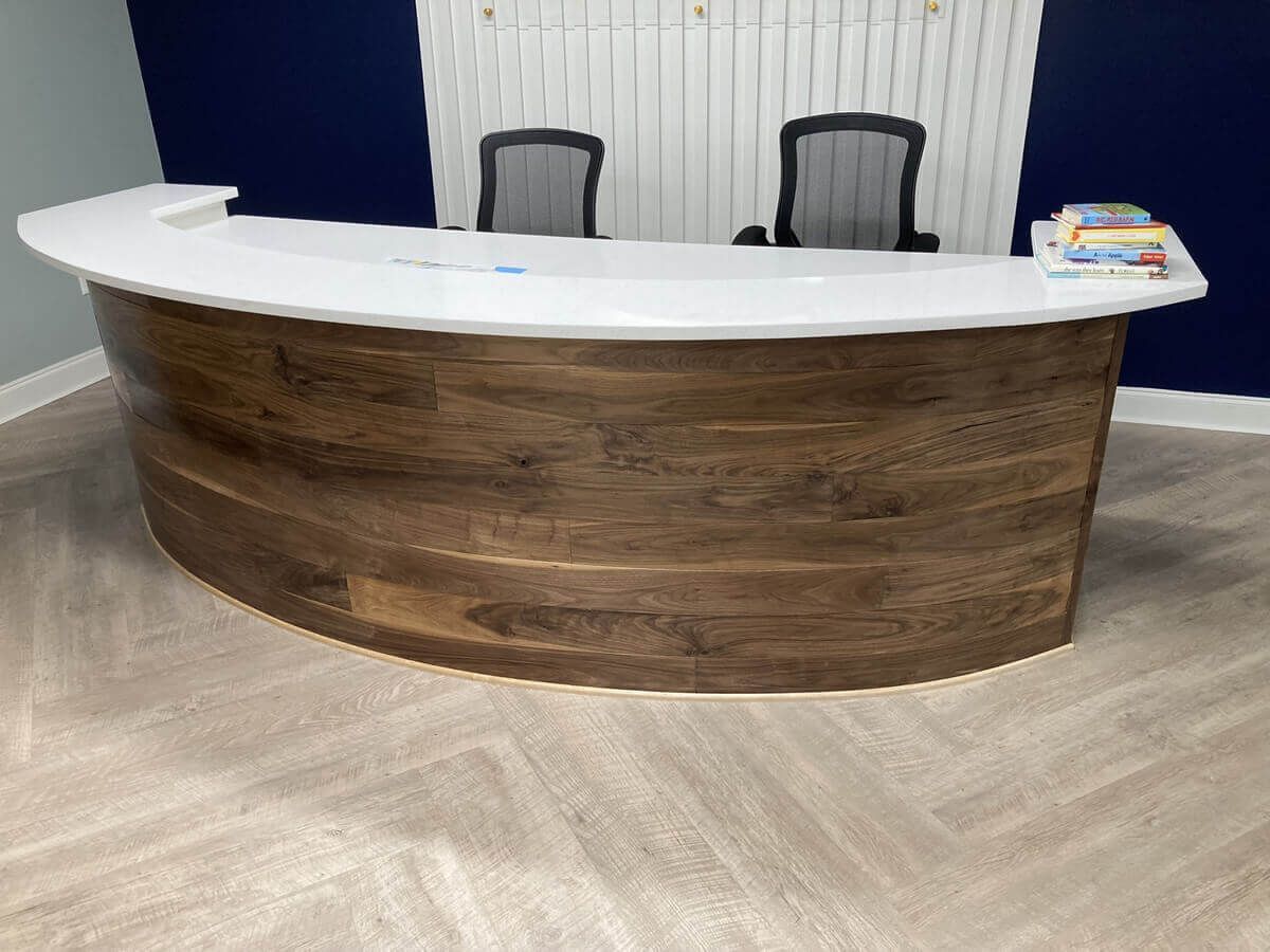 Curved wooden reception desk with white countertop and two chairs behind it in an office lobby