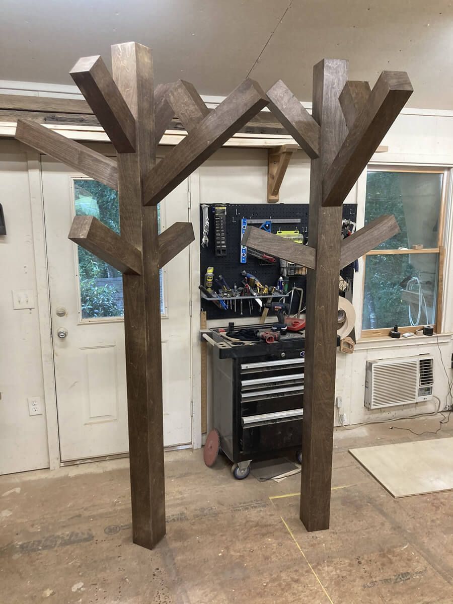 Wooden pergola-like frame structures inside a workshop or garage, with tools and windows in the background