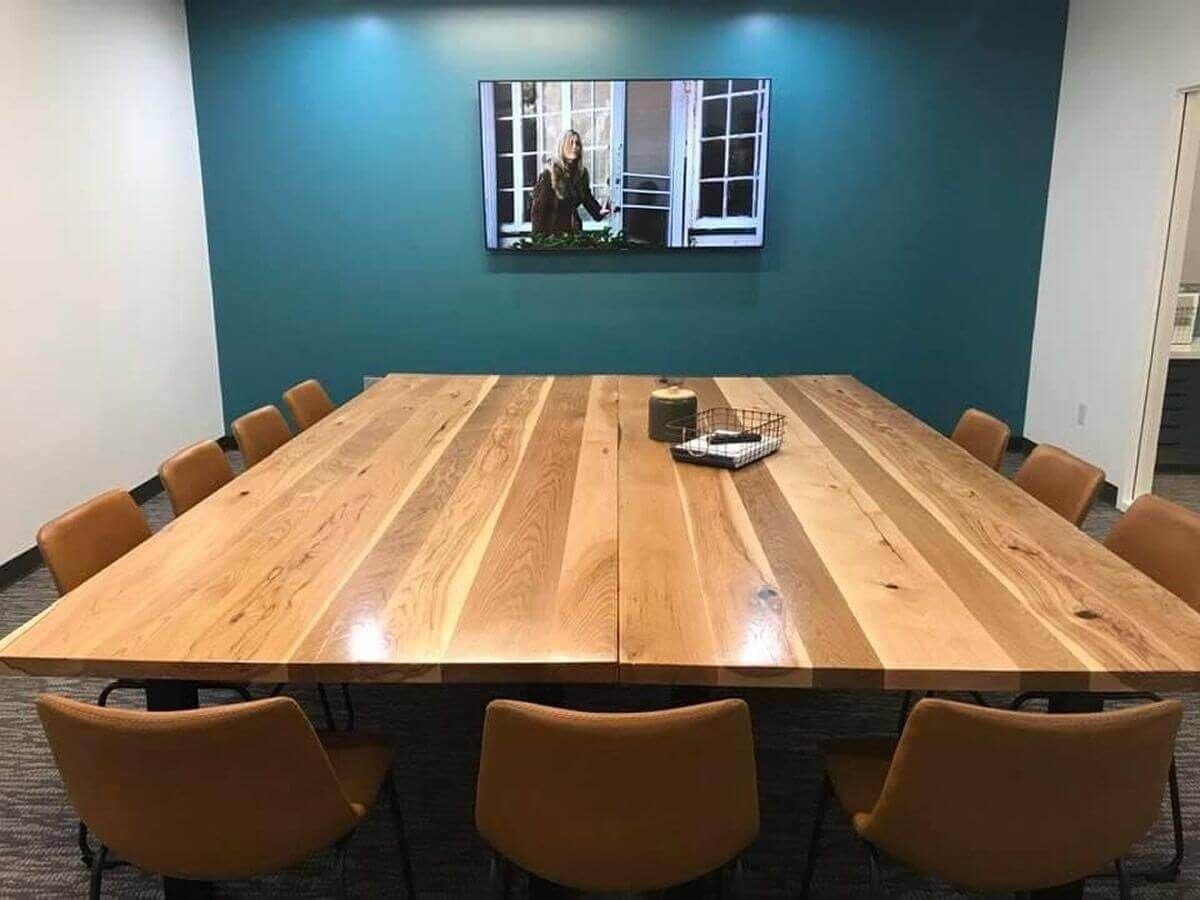 Modern conference room with a long wooden table, tan chairs, teal accent wall, and wall-mounted screen