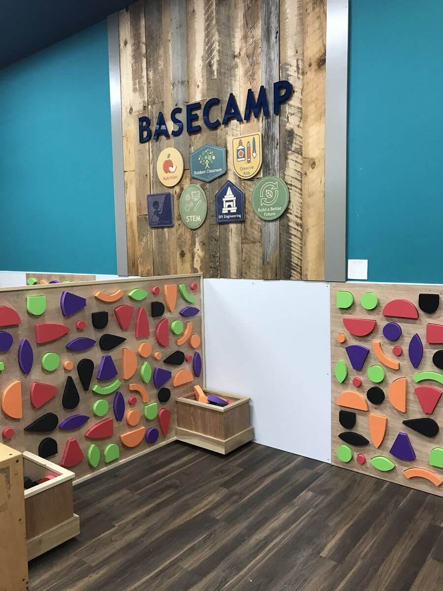 Indoor climbing play area with colorful bouldering walls and a “BASECAMP” sign on wood paneling