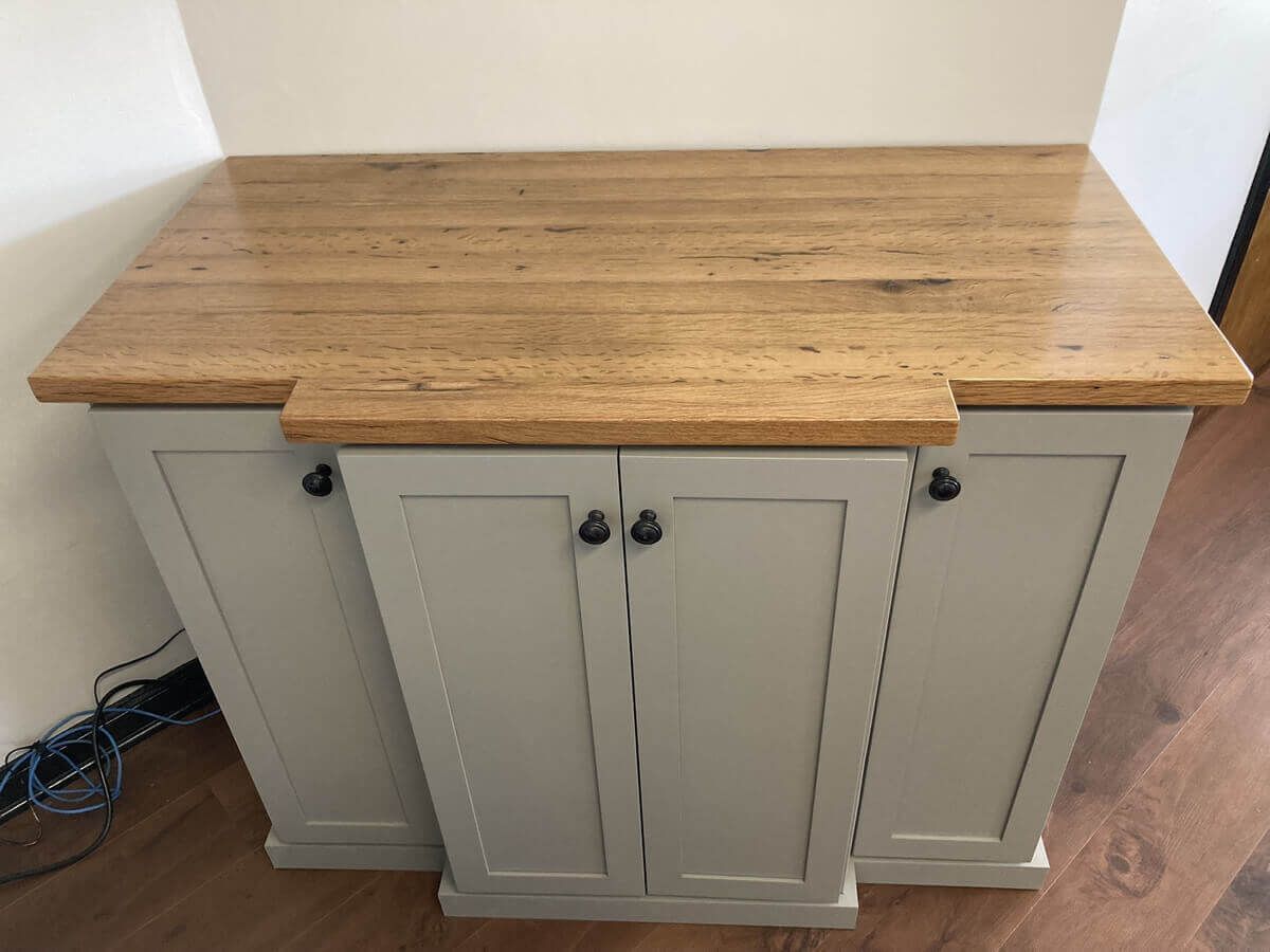 Gray cabinet with a wood countertop against a wall in a room corner