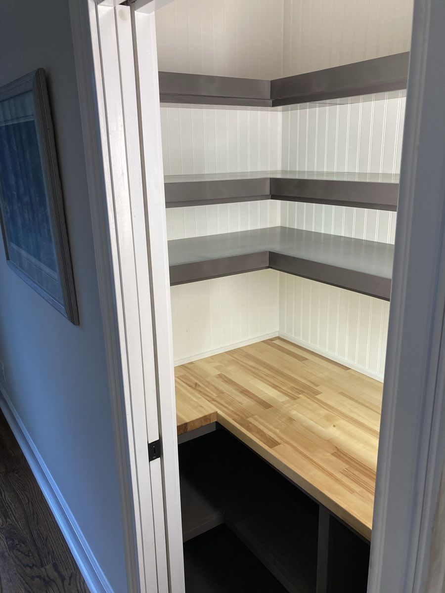 Small closet with white shelves and a wooden desk surface inside, viewed through an open doorway