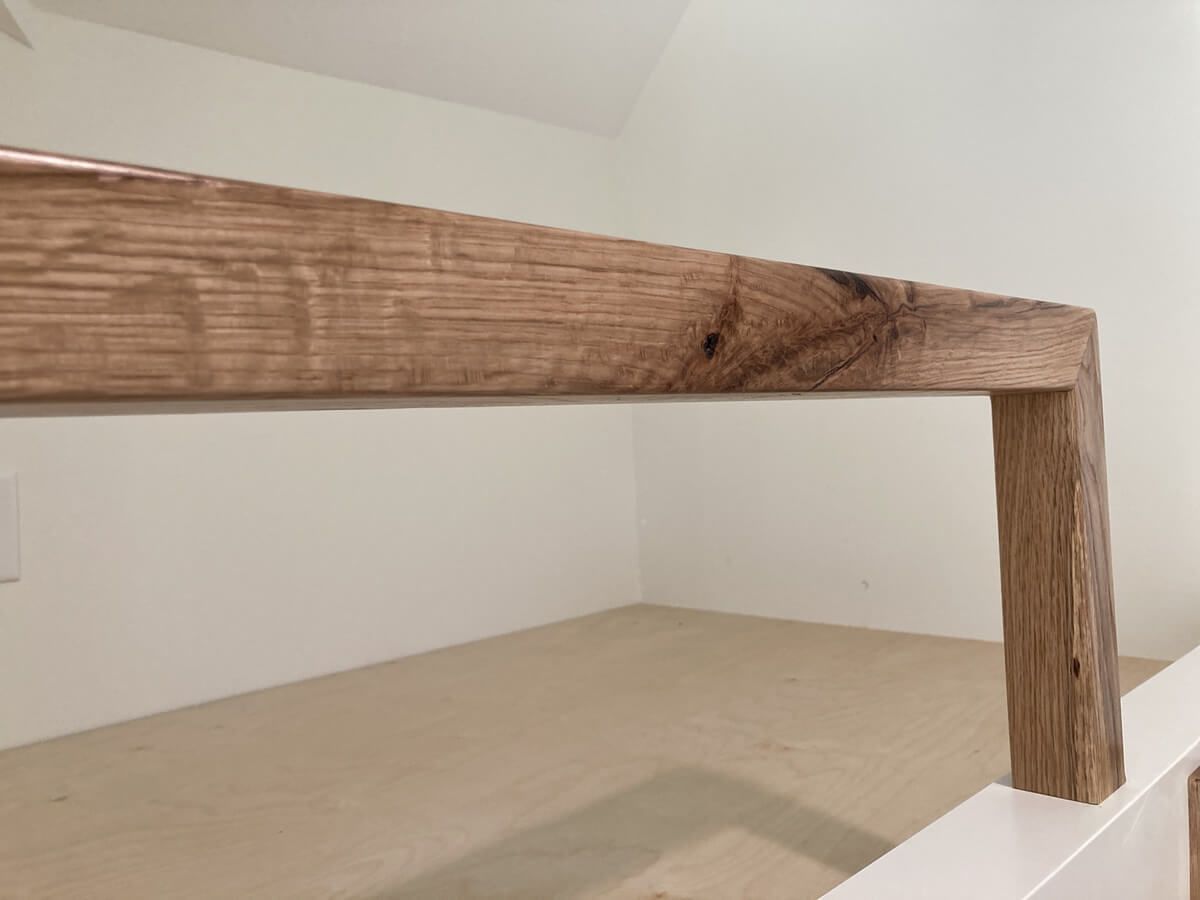 Wooden bench or table corner with a rough top and one vertical leg against a plain wall.
