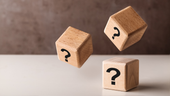 Three wooden blocks with question marks, one floating above two on a table.