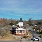 Small red-brick church with a white steeple beside a road on a clear day
