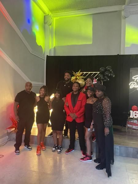 Group posing for a photo in a black-walled event space with colorful lights and a neon sign.
