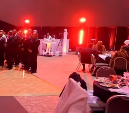 Guests mingling at a dimly lit banquet hall with red stage lights and tables set for dinner