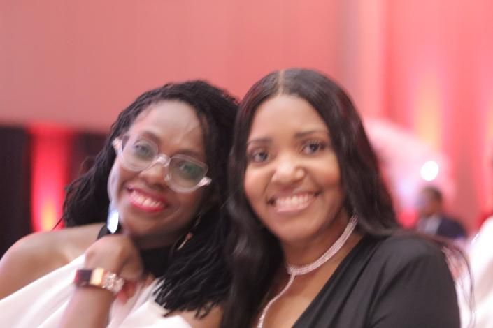 Two smiling people posing indoors with a pink-lit background.