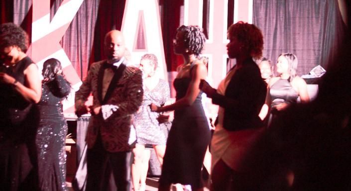 People standing on stage at an awards event, with pink lighting and dark curtains in the background