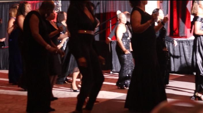 People dancing in a red-lit venue, with performers in black and silver outfits on stage