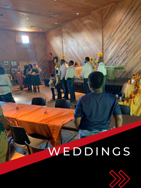 Wedding reception with guests standing near a decorated stage in a wood-paneled hall