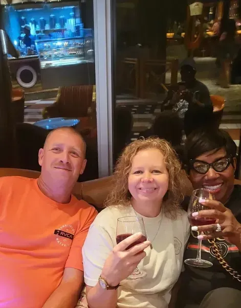 Three friends smiling and holding drinks at a dimly lit bar table.
