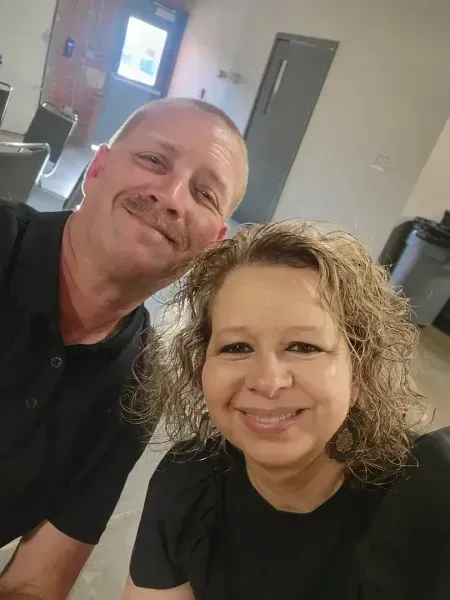 Two smiling people posing for a selfie indoors, wearing black shirts.