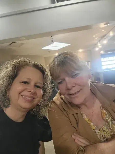 Two people smiling at a table indoors under warm ceiling lights