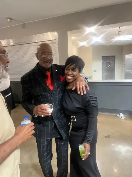 Three people posing indoors, smiling and holding drinks in a hallway.