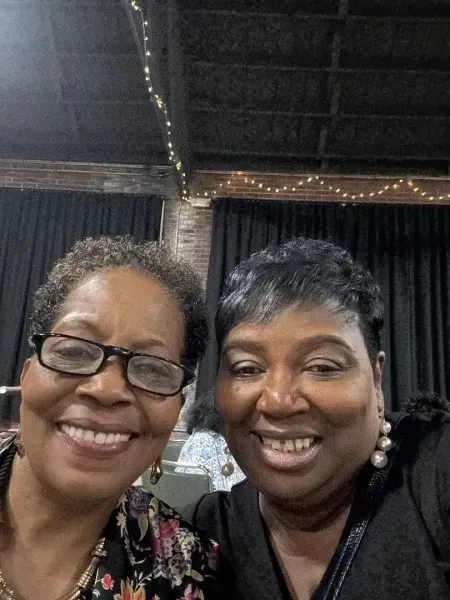 Two smiling women posing closely together in a dim indoor setting with string lights overhead