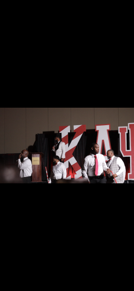 People on a stage holding a red-and-white flag in front of a large backdrop.