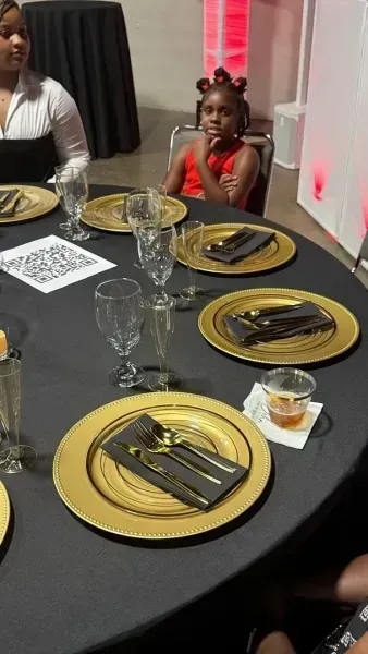 Decorated banquet table with black and gold place settings, glassware, and a QR code card at an event