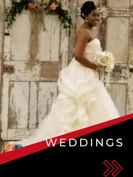 Bride in a white gown holding a bouquet, standing before rustic doors with floral decor and “WEDDINGS” text.