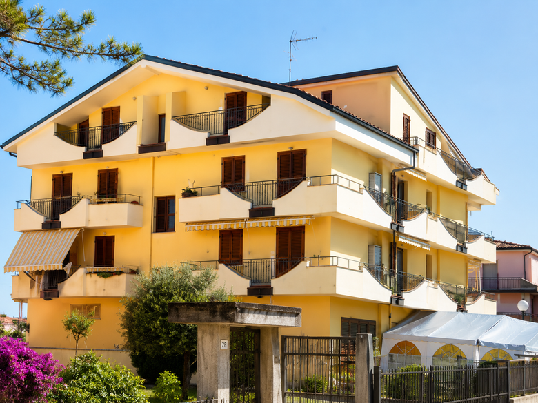 Patio di una villa moderna con lettini prendisole e una piscina blu sotto un cielo luminoso.