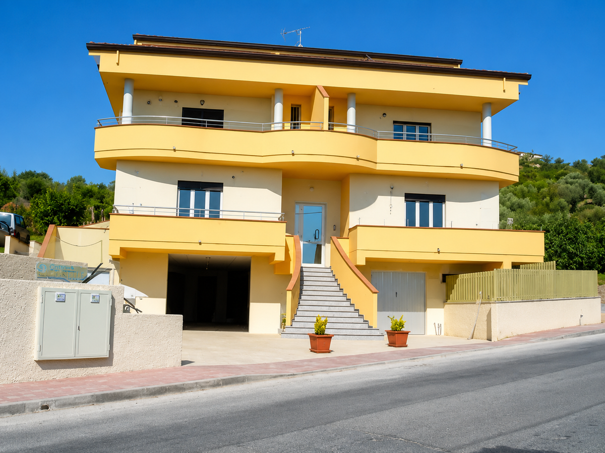 Casa gialla a tre piani con balconi affacciata su una strada in una giornata di sole.