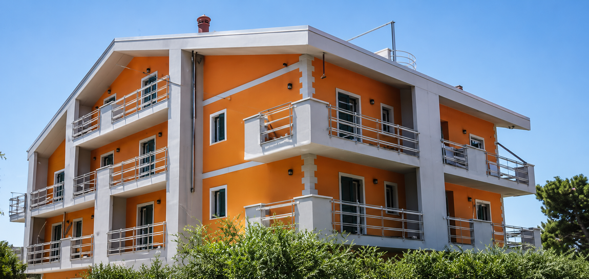 Edificio residenziale arancione a tre piani con balconi, porte da garage e vialetto d'accesso con cancello.