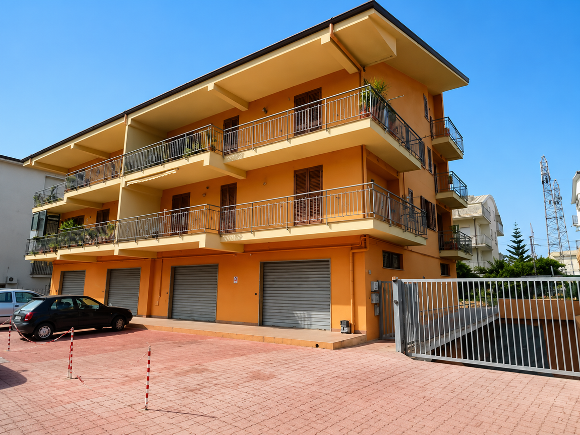 Edificio residenziale arancione a tre piani con balconi, porte da garage e vialetto d'accesso con cancello.