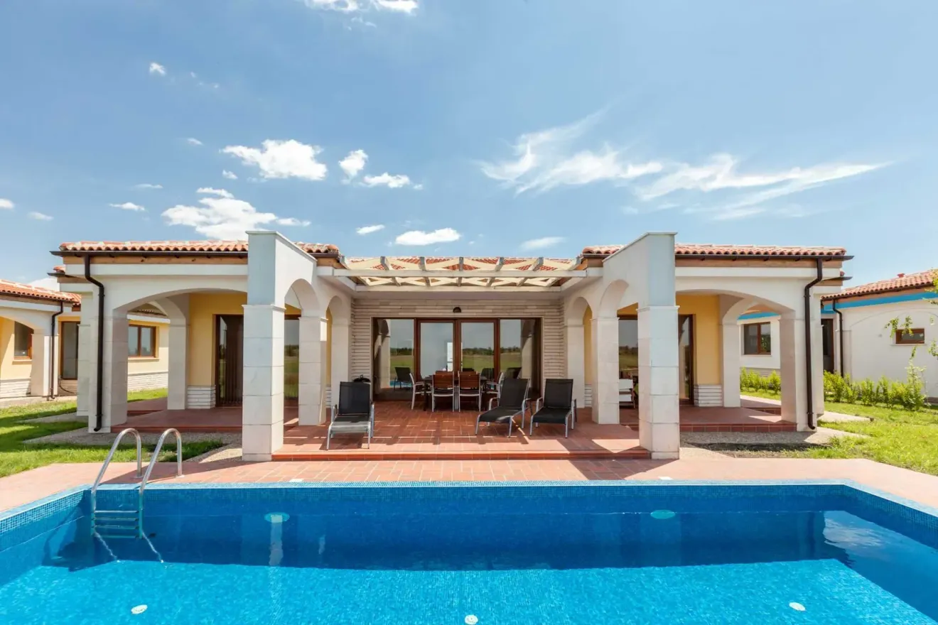 Villa moderna con patio coperto e lettini prendisole a bordo piscina.