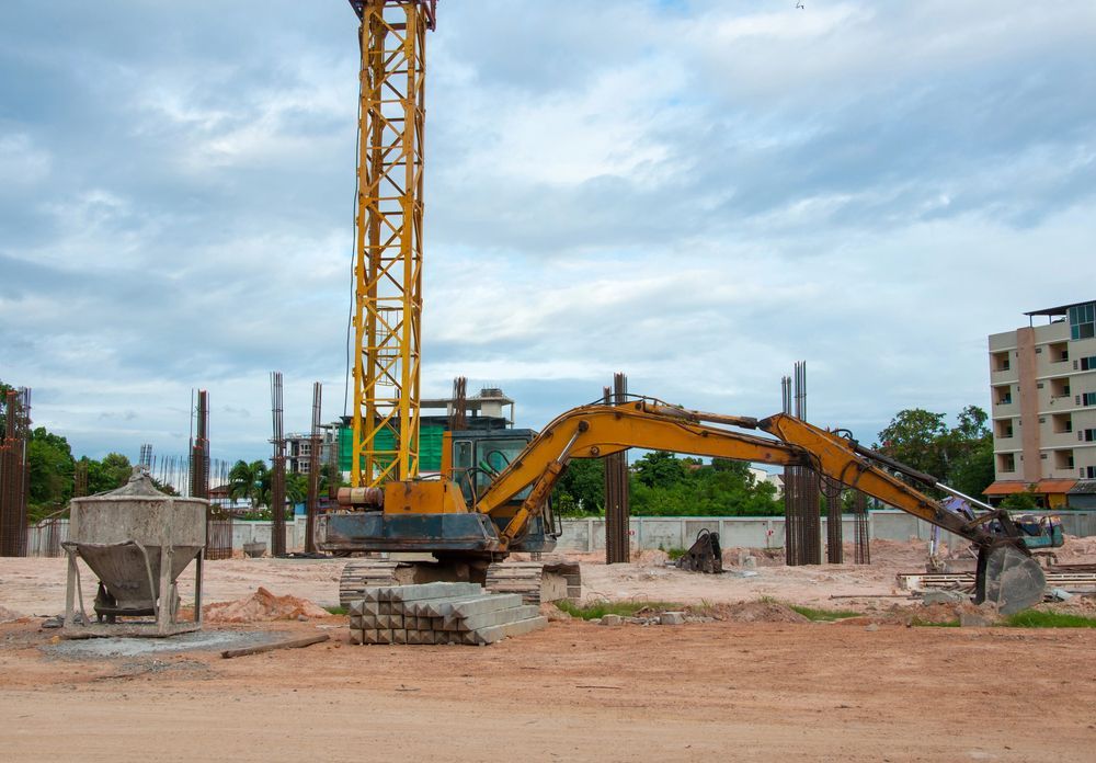 Un escavatore giallo in un cantiere edile sotto un cielo nuvoloso.