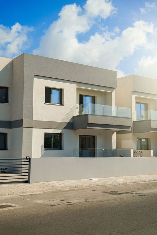 Casa moderna a due piani color beige con balcone e parete bianca sotto un cielo azzurro