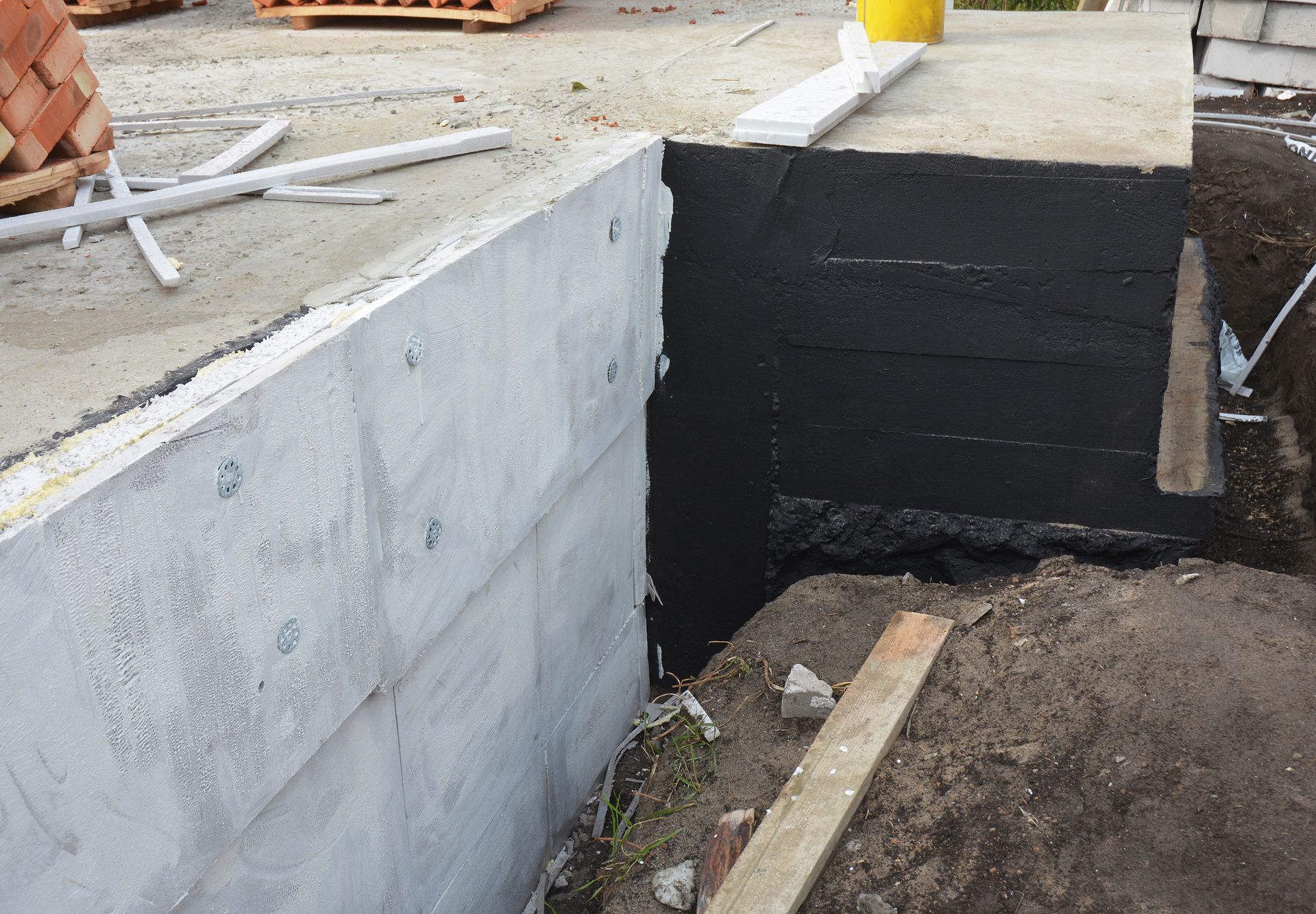 Partially built concrete foundation wall with black waterproofing and dirt trench beside it