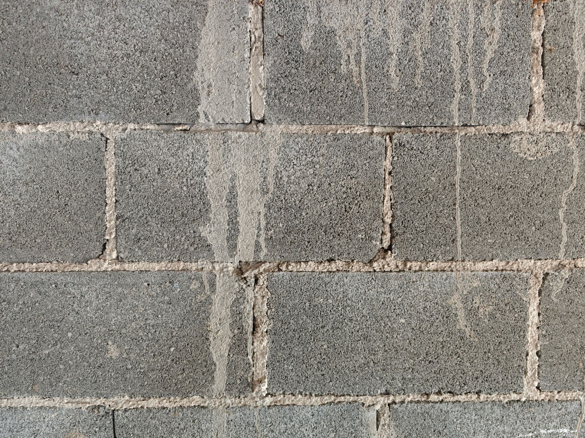 Close-up of a gray concrete block wall with worn mortar and vertical water stains Close-up of a gray concrete block wall with worn mortar and vertical water stains