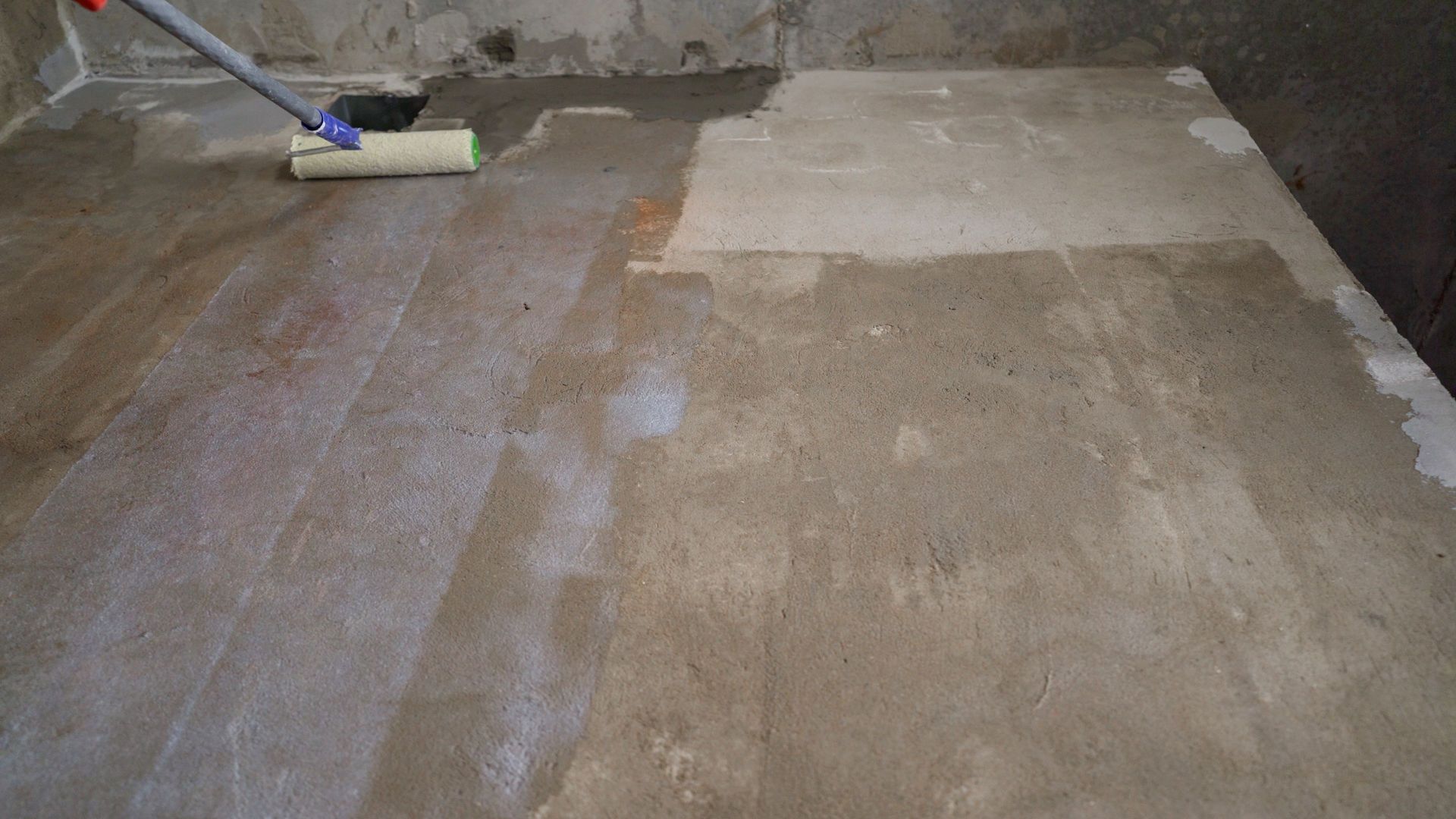 Concrete floor being cleaned with a mop, showing wet and dry patches.