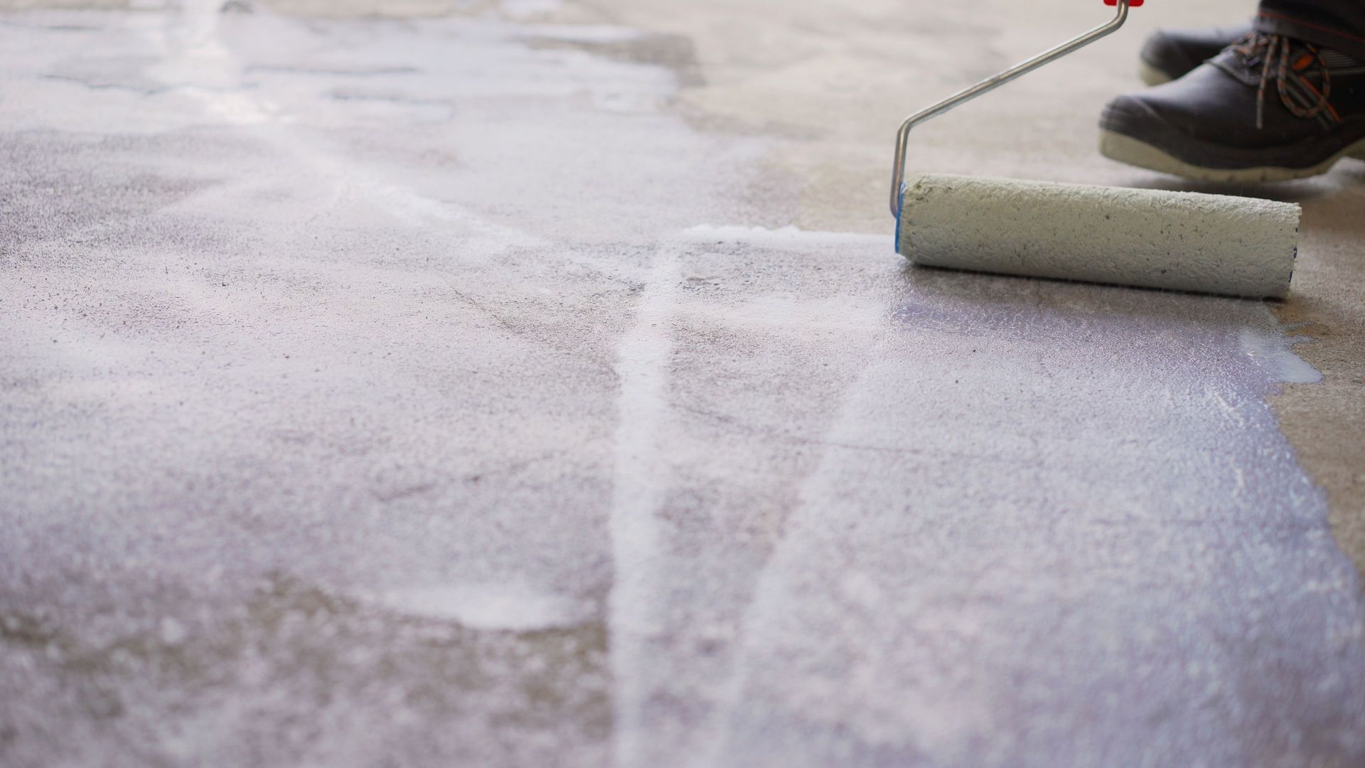 Paint roller applying white coating to a floor surface during painting work