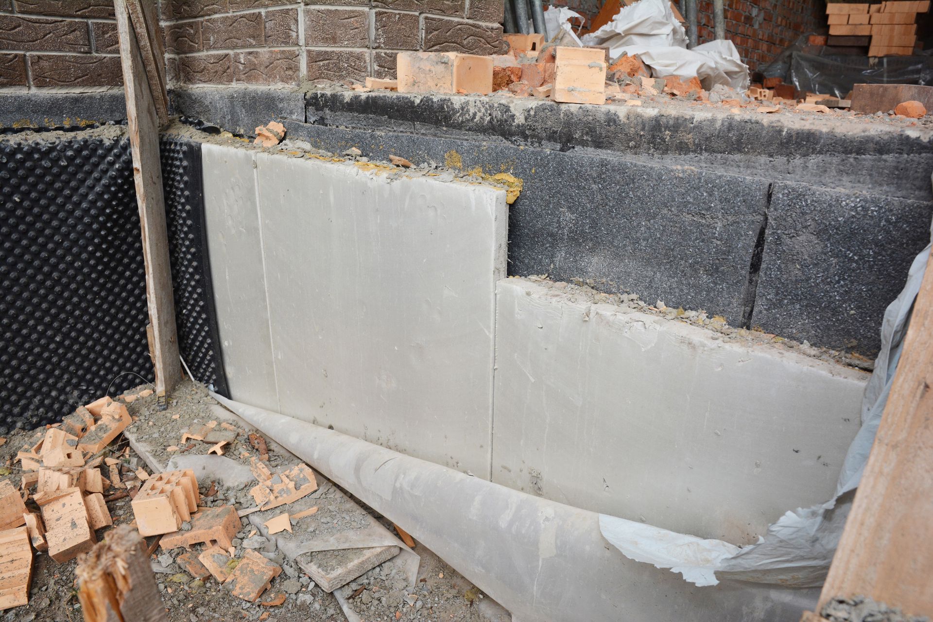 Partially finished brick wall with gray insulation panels and debris at a construction site