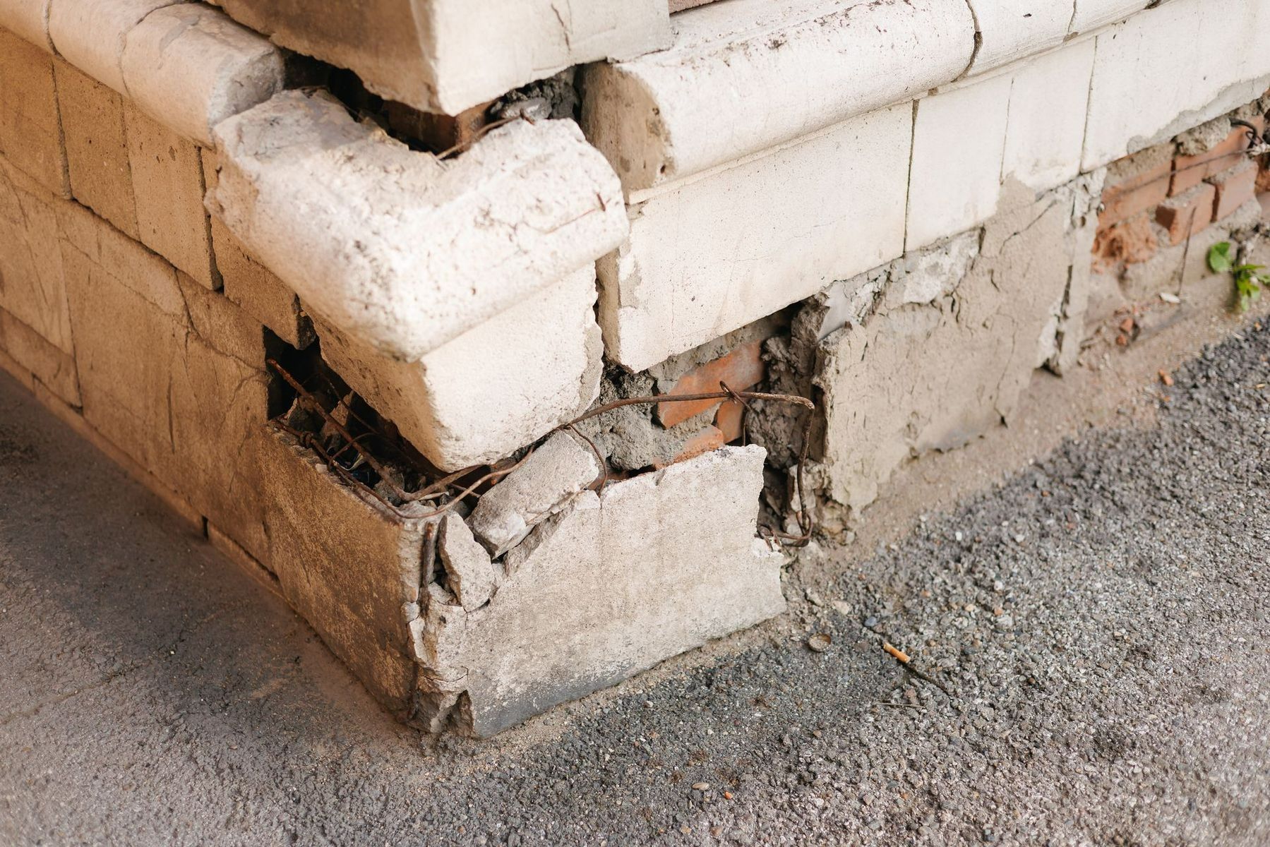 Cracked and damaged white stone corner on a building foundation beside gravel ground