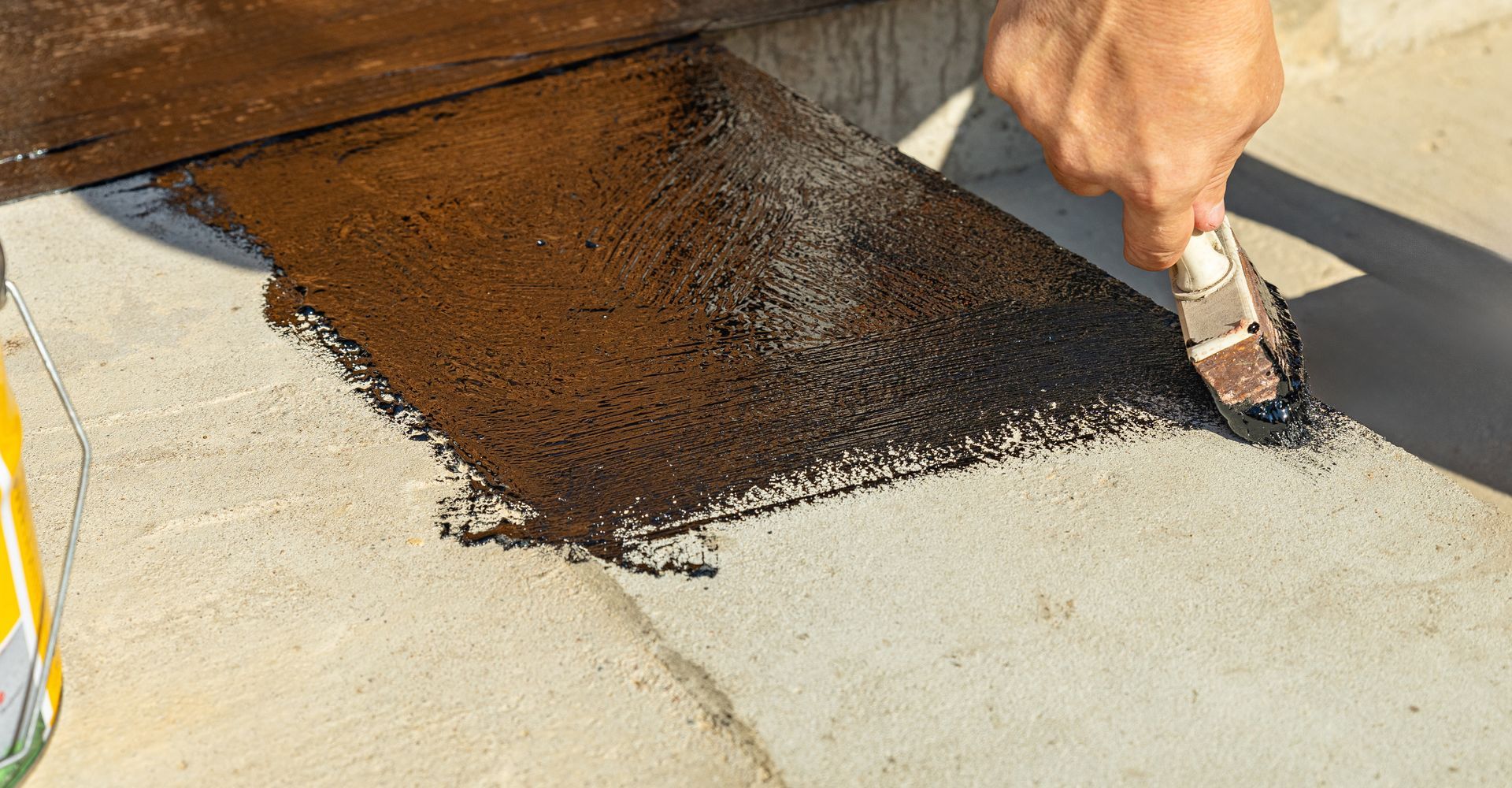 Hand spreading black roof coating on a flat roof with a brush and roller