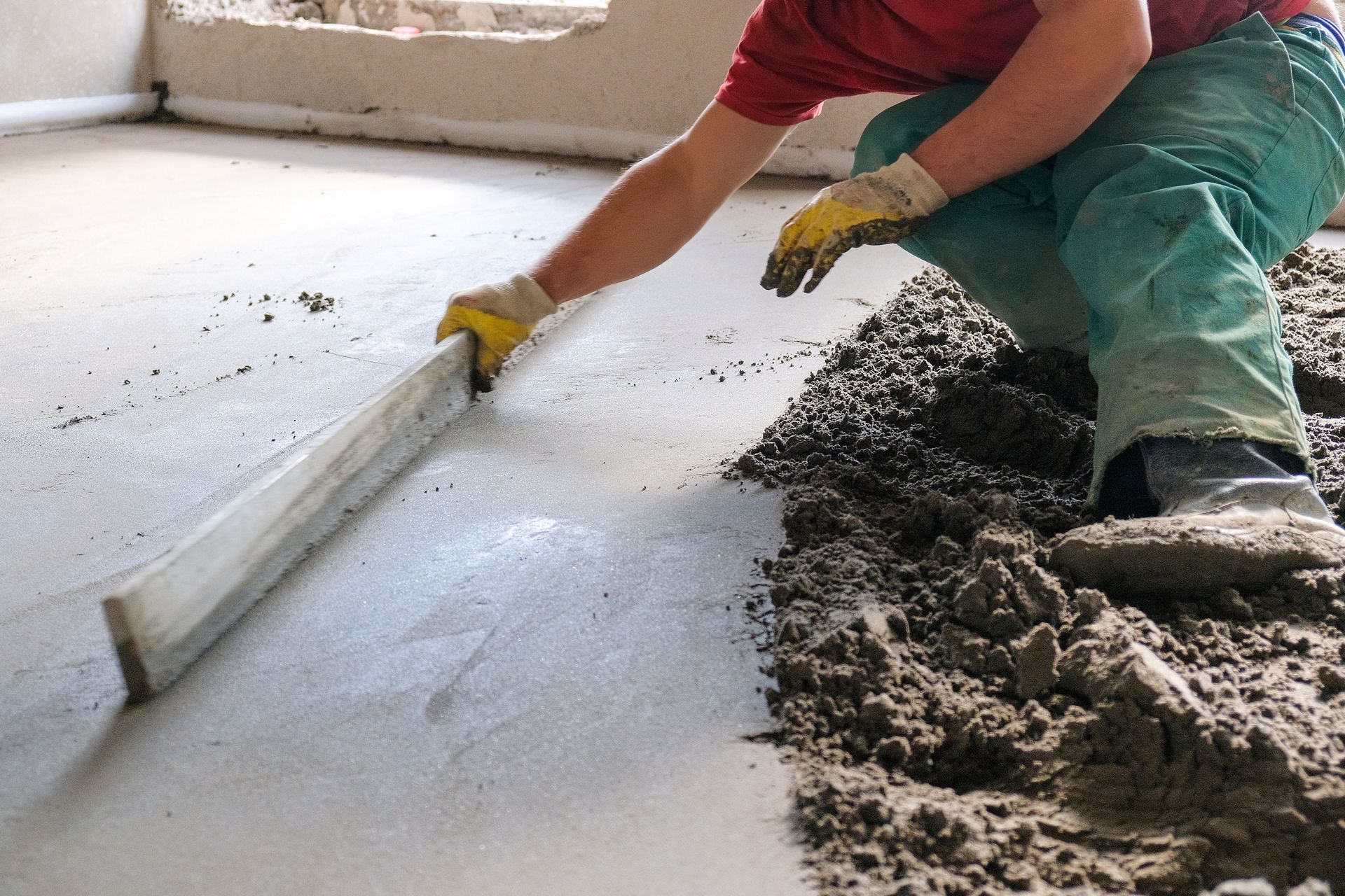 Worker smoothing wet concrete floor with a trowel indoors