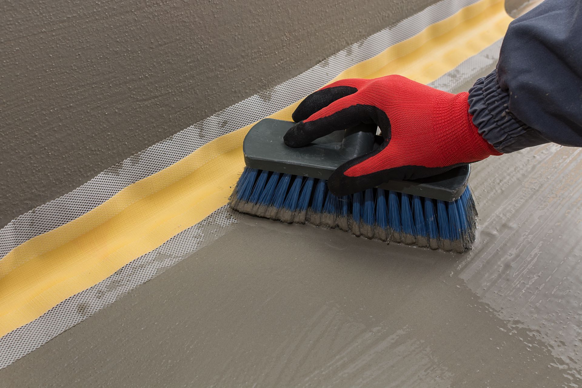 Worker brushing waterproof sealant over mesh-taped wall and floor joint. Worker brushing waterproof sealant over mesh-taped wall and floor joint.