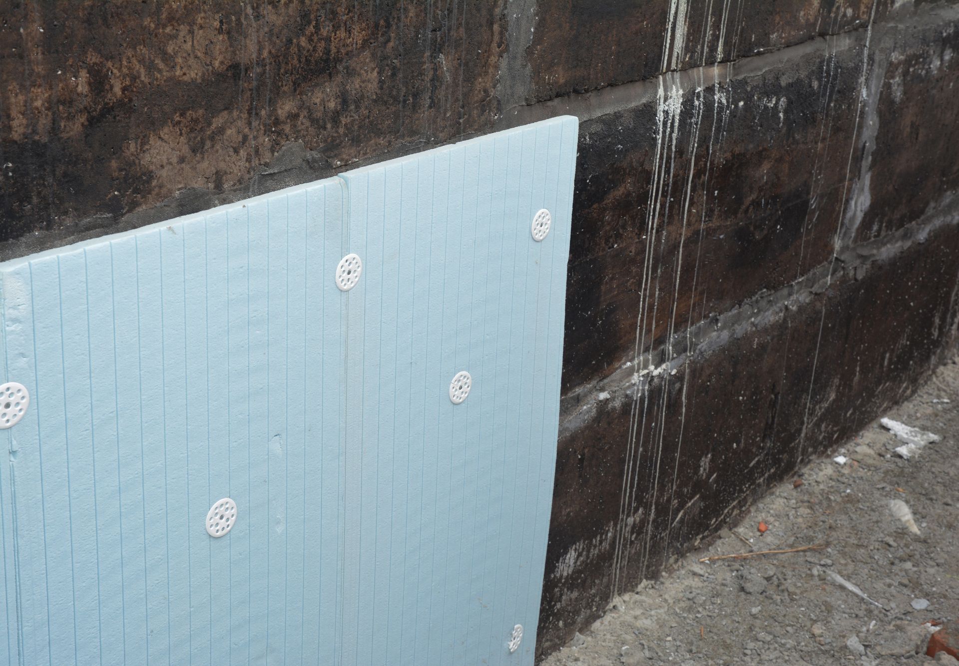 Blue insulation board fixed to a rough dark wall near a concrete floor.