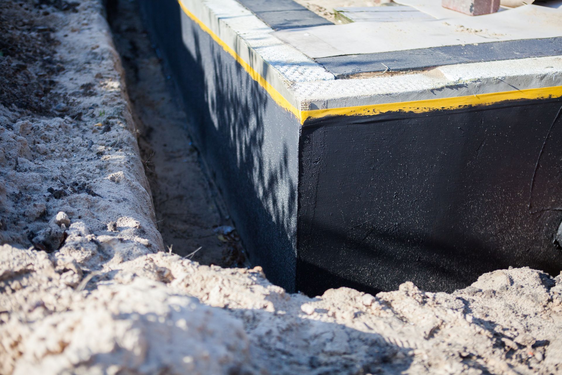 Excavated foundation wall with black waterproof membrane and drainage board.