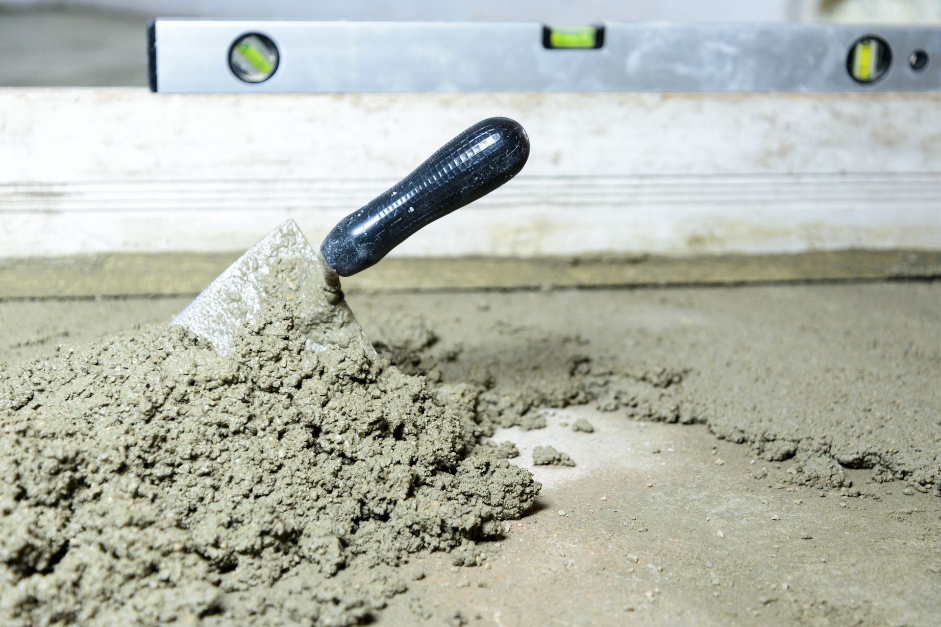 Trowel spreading wet concrete on a floor, with a spirit level in the background.