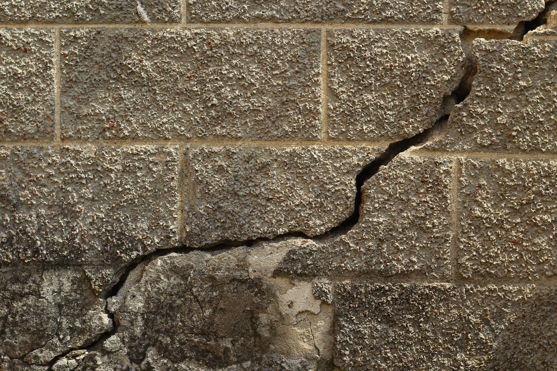 Cracked gray cinder block wall with a diagonal fracture running across the center