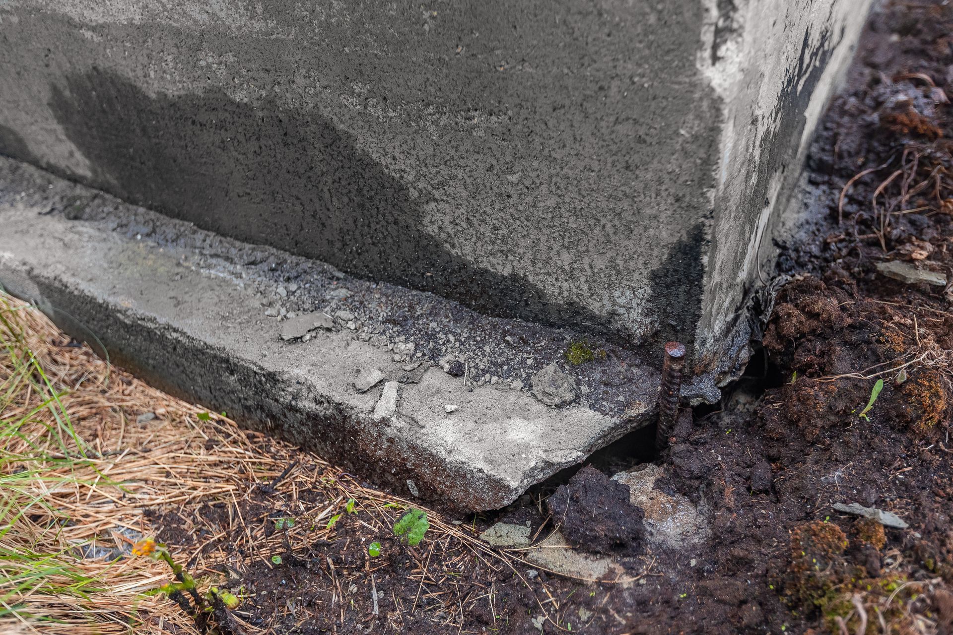 Cracked concrete foundation corner with a damaged base and exposed soil nearby