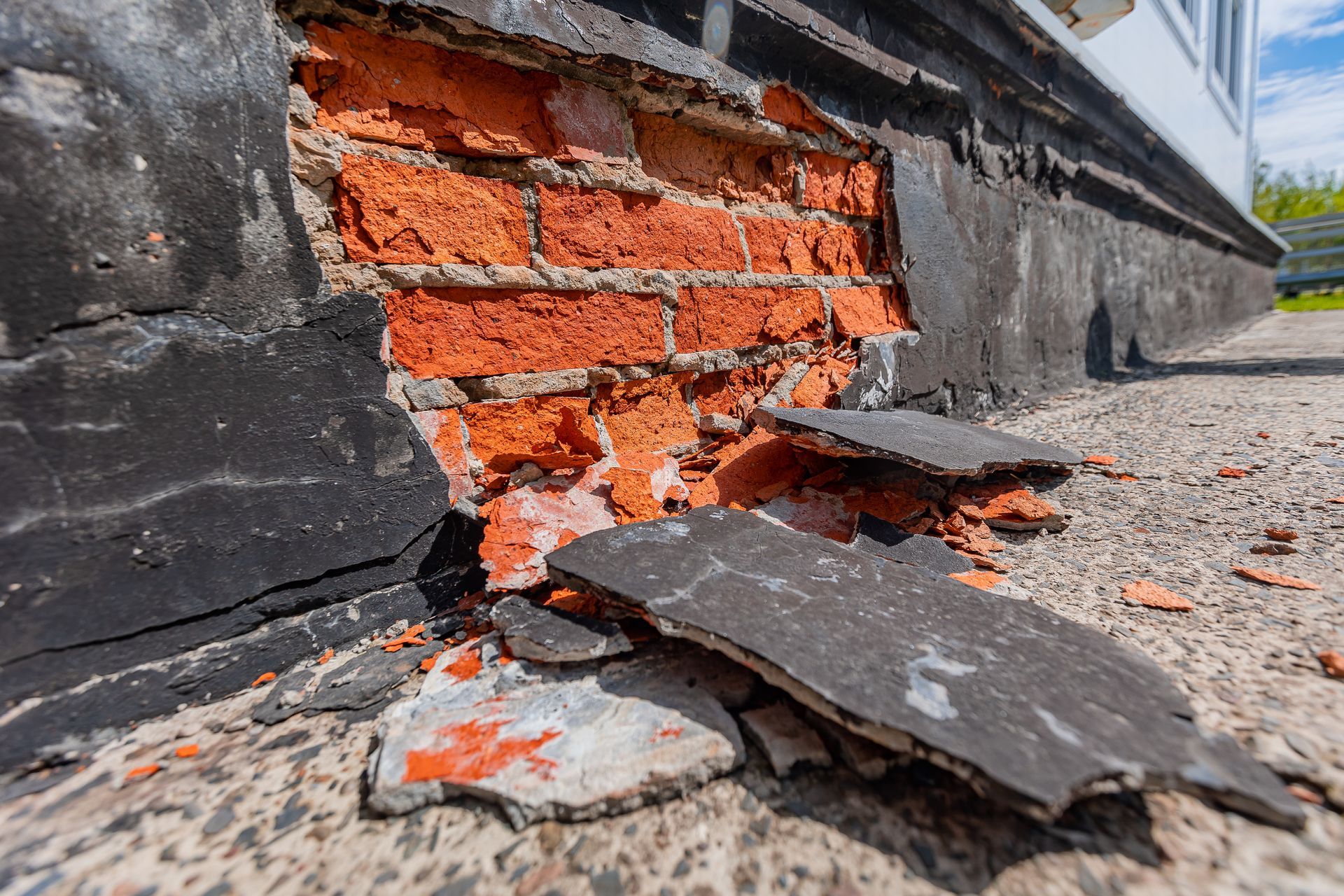 Cracked brick wall with peeling black paint and broken bricks on a sidewalk