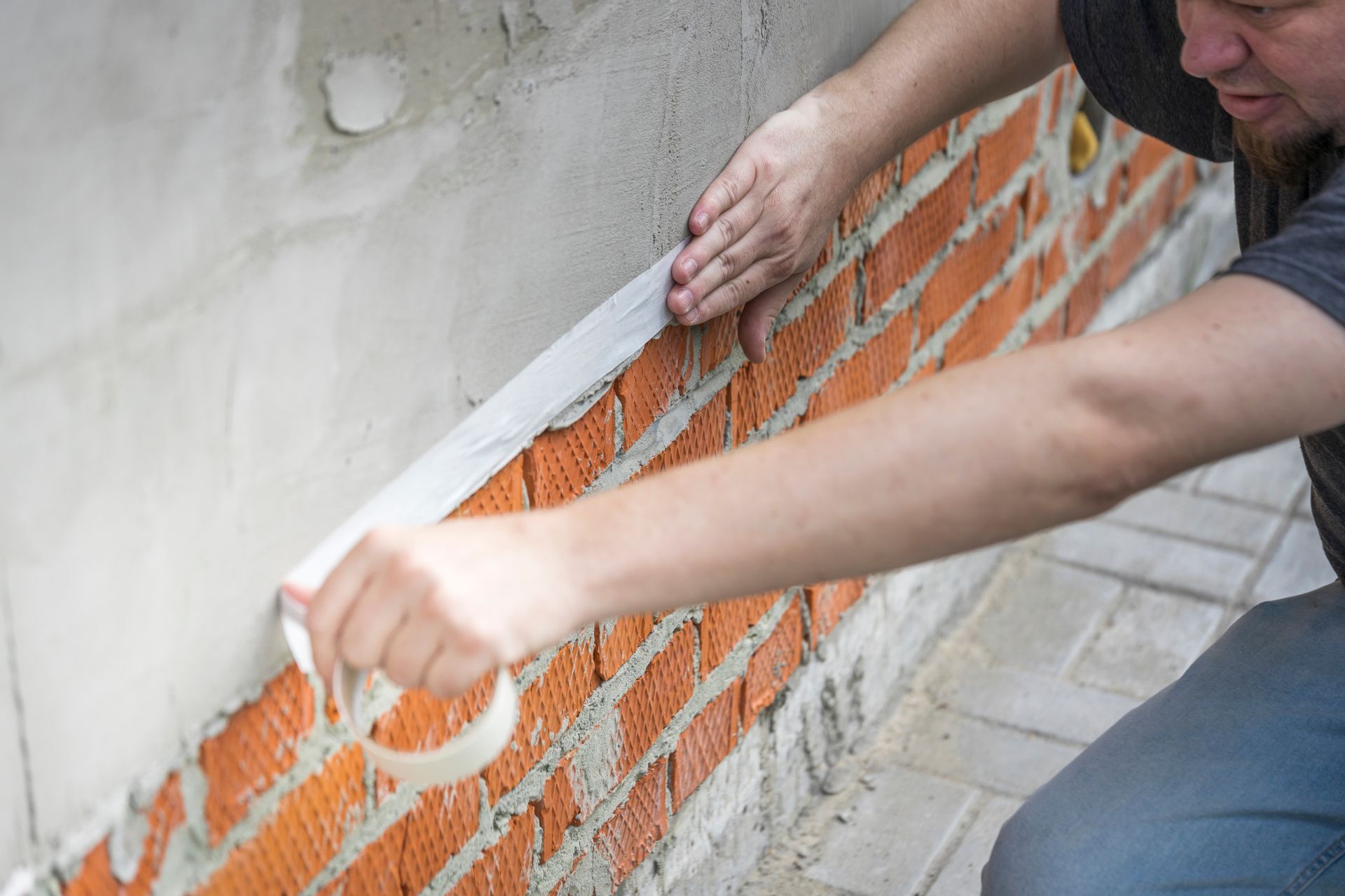 Person applying white trim to an orange brick wall during home construction Person applying white trim to an orange brick wall during home construction