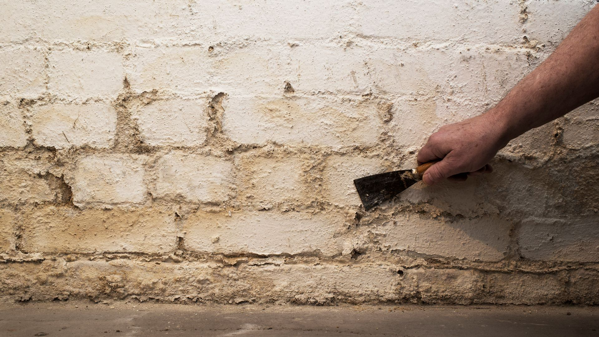 Hand scraping white paint or plaster from a dirty brick wall with a putty knife