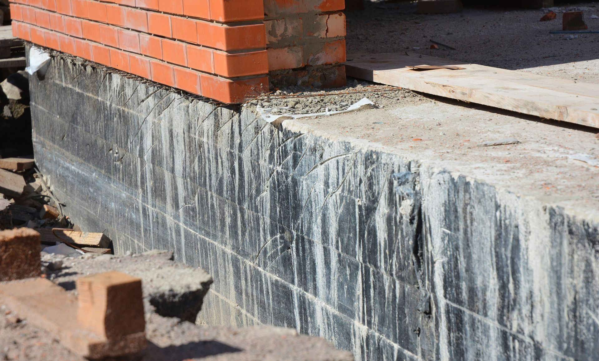 New brick wall on concrete footing with white water stains and a partially paved ground nearby
