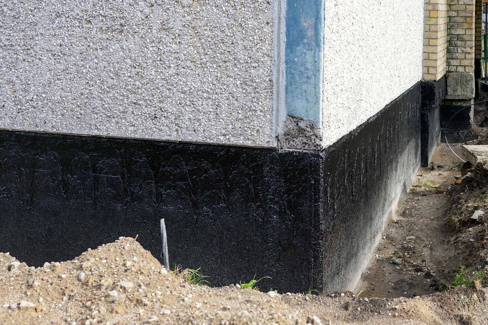 Corner of a building with a black-painted foundation and dirt construction debris beside it