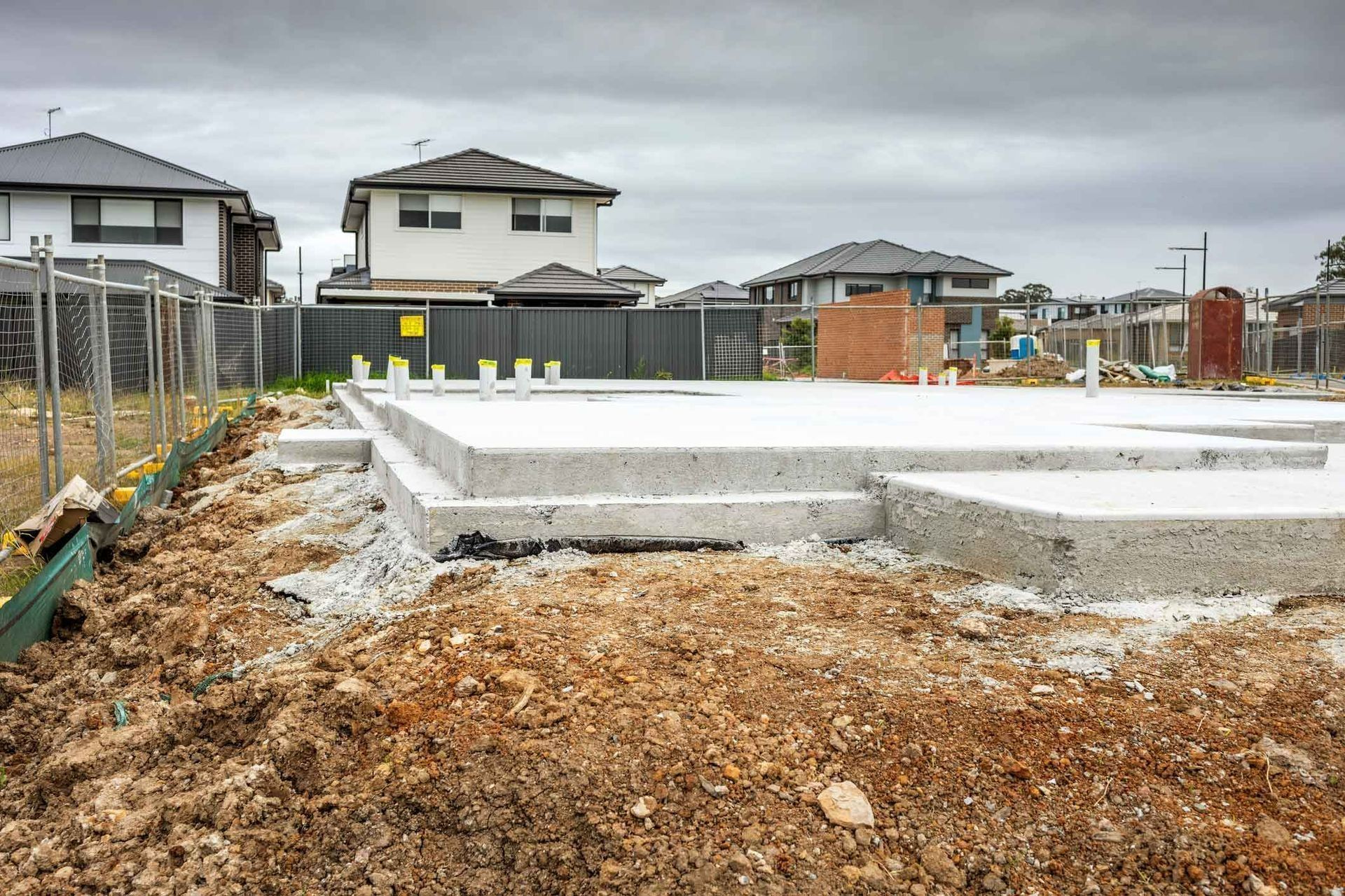 Foundation slab under construction in a new housing development, with dirt and fenced lots on an overcast day Foundation slab under construction in a new housing development, with dirt and fenced lots on an overcast day